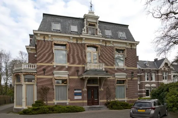 Het pand van Haarhuis Hammer aan de Dr. Nassaulaan in Assen: een statige villa van rode en gele baksteen met een leien mansardedak en witte sierlijsten.